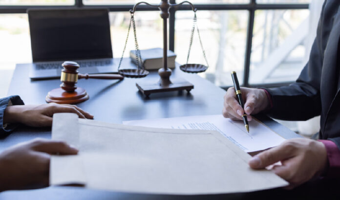 a imagem mostra o símbolo da justiça na mesa e um homem assinando um documento