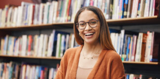 mulher sorrindo segurando um livro em uma biblioteca