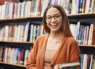 mulher sorrindo segurando um livro em uma biblioteca