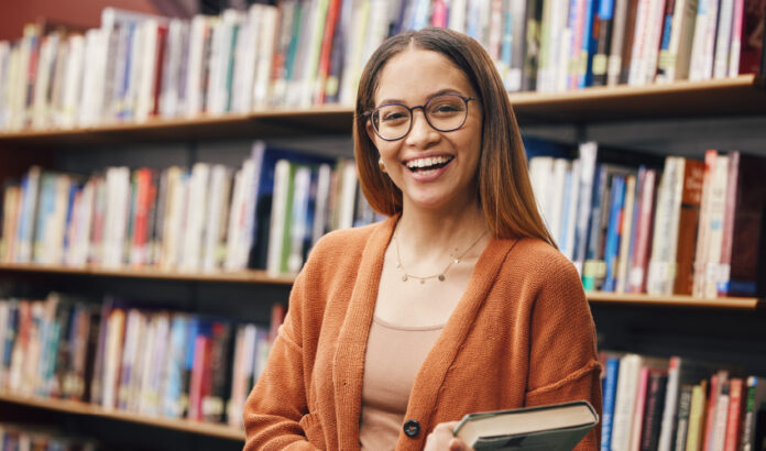 mulher sorrindo segurando um livro em uma biblioteca