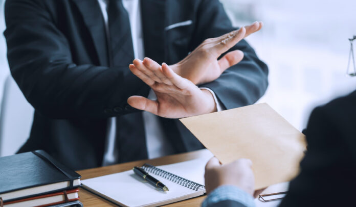 Homem vestido de terno se recusa a assinar contrato e faz um sinal negativo com a mão