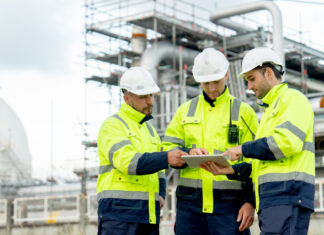 Engenheiros estão em frente à fábrica petroquímica e usam tablet para discutir seu trabalho.